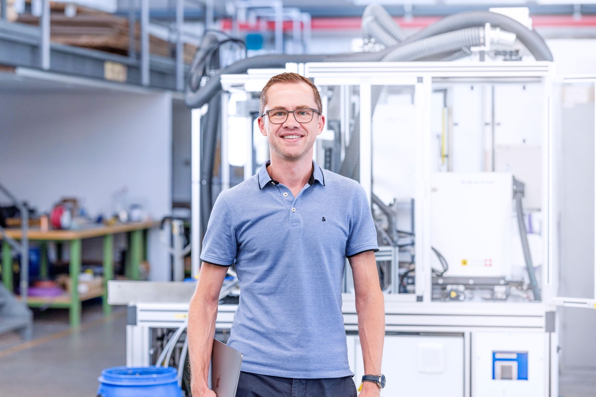Ein Mann steht vor einer Maschine in einer Fabrik und hält ein blaues Fass.