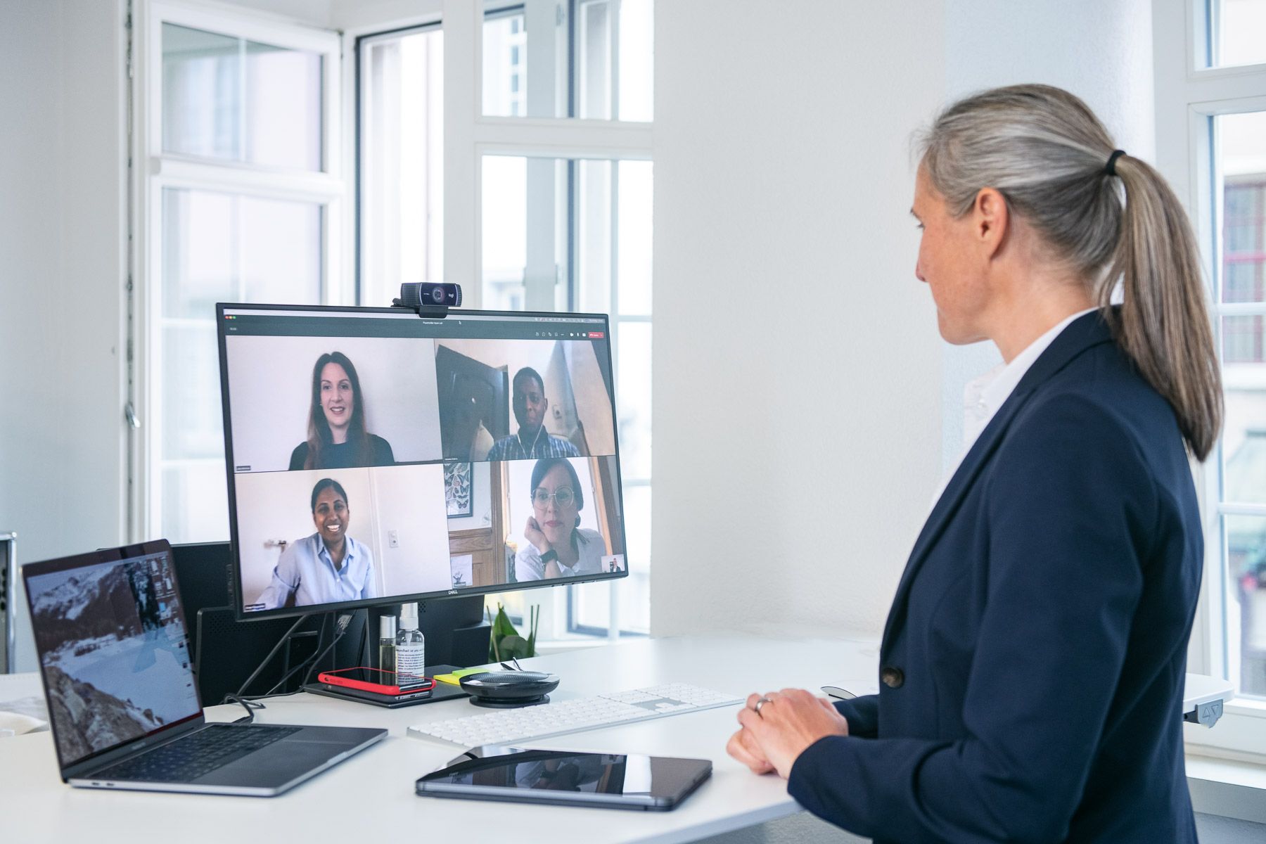 A woman is sitting at a desk looking at a computer screen with a group of people on it.
