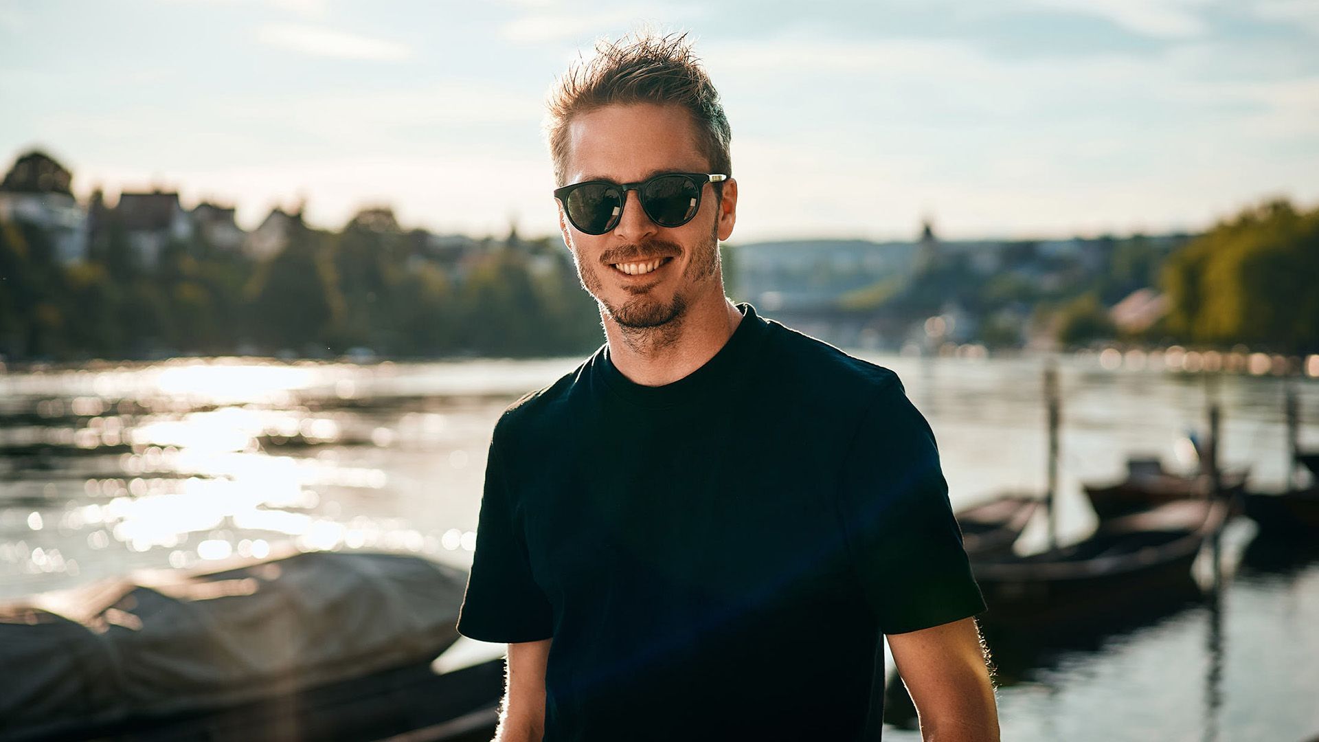 A man wearing sunglasses is standing in front of a body of water.